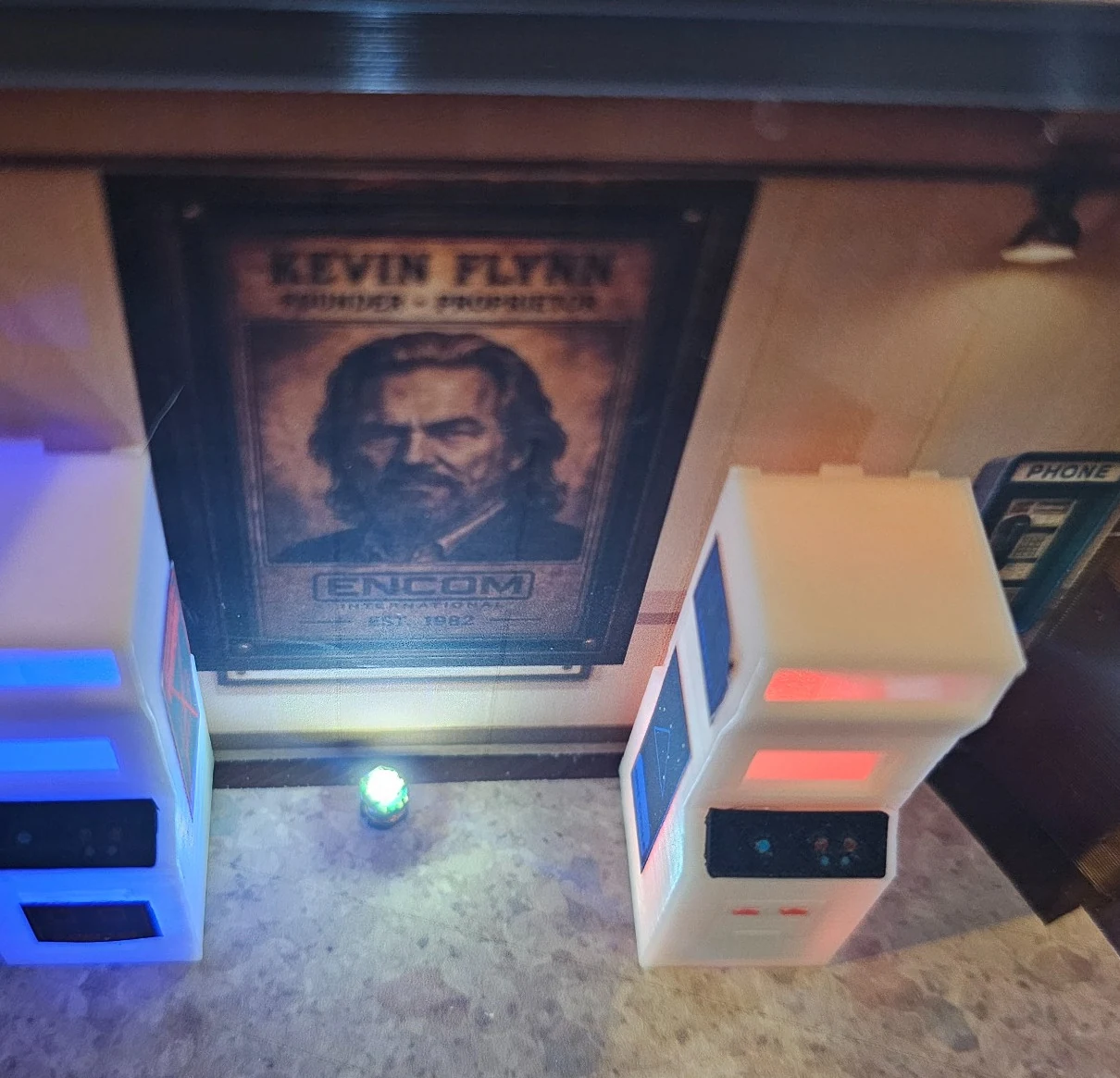 Photograph of the real miniature Flynn wall with portrait, payphone and illuminated arcade machines